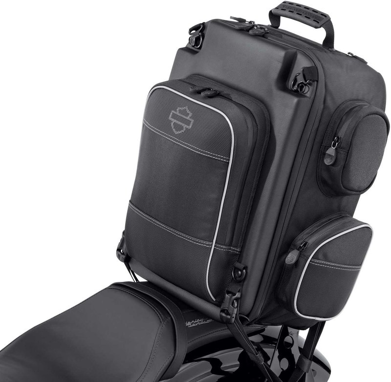 Harley-Davidson Accessories Onyx Premium Luggage Weekender Bag. Part of the Onyx Premium Luggage Collection, this backpack-style Weekender Bag suits around-town use or a weekend getaway. The cavernous main compartment holds a pair of boots, a change of clothes, an extra jacket or sweatshirt and spare gloves and hats. It includes a padded laptop compartment and two further padded pockets for small electronics. Outside there are two pockets (one felt-lined for eyewear), a drawbridge-style front compartment for pens and documents, and four side pockets for chargers, keys and other small items. The mounting straps tuck away into a built-in storage pouch for a clean look, and stowable backpack straps with raised back padding make it comfortable to carry. Made of premium 1680-denier UV-stable ballistic polyester that stands up to tough road and weather conditions without fading. Features water-resistant zippers with glove-friendly pulls, a burnt-orange interior for easy visibility, MOLLE-style webbing for modular pouch attachment, a non-slip abrasion-resistant base and reflective piping. Dimensions: 18" W x 11.5" D x 18" T. Capacity: 1,800 cubic inches. Includes a rain cover with an elastic hem and barrel-lock mechanism that stays put at highway speeds.