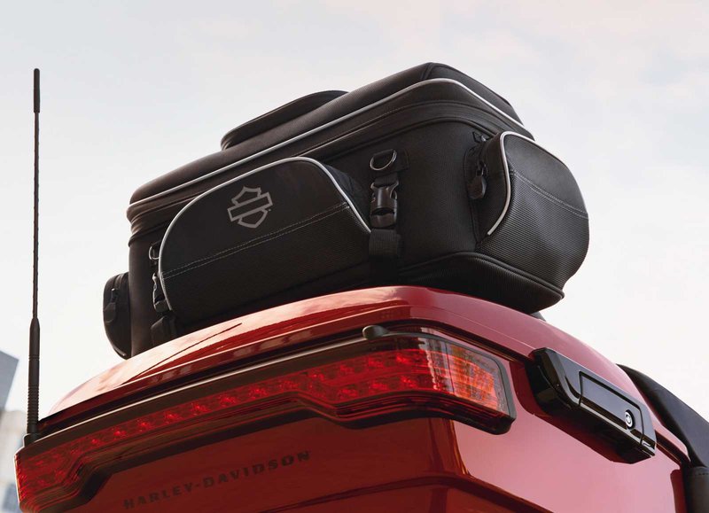 Harley-Davidson Accessories Onyx Premium Luggage Tour-Pak Rack Bag. Part of the Onyx Premium Luggage Collection, this bag is designed to sit atop most Tour-Pak luggage racks, adding storage for long trips. The main compartment features three mesh pockets for organisation and enough space for clothes on a short trip. Outside, the top zip pocket is fleece-lined for protective eyewear storage, while the front, back and side pockets suit gloves, keys, cords and a phone charger. Dual side-carry handles, a rubber top handle and a detachable shoulder strap make off-bike transport easy, and rigid construction keeps the bag in shape even when empty. Made of premium 1680-denier UV-stable ballistic polyester that stands up to tough road and weather conditions without fading. Features water-resistant zippers with glove-friendly pulls, a burnt-orange interior for easy visibility, MOLLE-style webbing for modular pouch attachment, a non-slip abrasion-resistant base and reflective piping. Dimensions: 24" W x 14" D x 10.4" T. Capacity: 2,600 cubic inches (42 litres). Includes a removable shoulder strap and a rain cover with an elastic hem and barrel-lock mechanism that stays put at highway speeds. Fits models equipped with Tour-Pak luggage racks (except FLRT and FLHXXX, or Mini Rack P/N 53100-96).