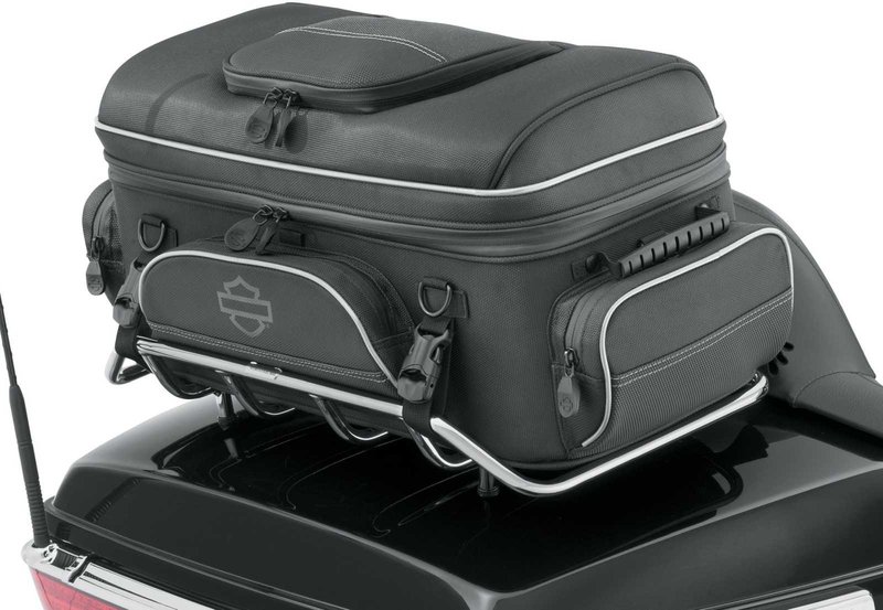 Harley-Davidson Accessories Onyx Premium Luggage Tour-Pak Rack Bag. Part of the Onyx Premium Luggage Collection, this bag is designed to sit atop most Tour-Pak luggage racks, adding storage for long trips. The main compartment features three mesh pockets for organisation and enough space for clothes on a short trip. Outside, the top zip pocket is fleece-lined for protective eyewear storage, while the front, back and side pockets suit gloves, keys, cords and a phone charger. Dual side-carry handles, a rubber top handle and a detachable shoulder strap make off-bike transport easy, and rigid construction keeps the bag in shape even when empty. Made of premium 1680-denier UV-stable ballistic polyester that stands up to tough road and weather conditions without fading. Features water-resistant zippers with glove-friendly pulls, a burnt-orange interior for easy visibility, MOLLE-style webbing for modular pouch attachment, a non-slip abrasion-resistant base and reflective piping. Dimensions: 24" W x 14" D x 10.4" T. Capacity: 2,600 cubic inches (42 litres). Includes a removable shoulder strap and a rain cover with an elastic hem and barrel-lock mechanism that stays put at highway speeds. Fits models equipped with Tour-Pak luggage racks (except FLRT and FLHXXX, or Mini Rack P/N 53100-96).